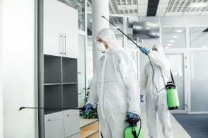 Commercial pest control workers in hazmat suits disinfect an office interior to maintain a safe, pest-free workspace